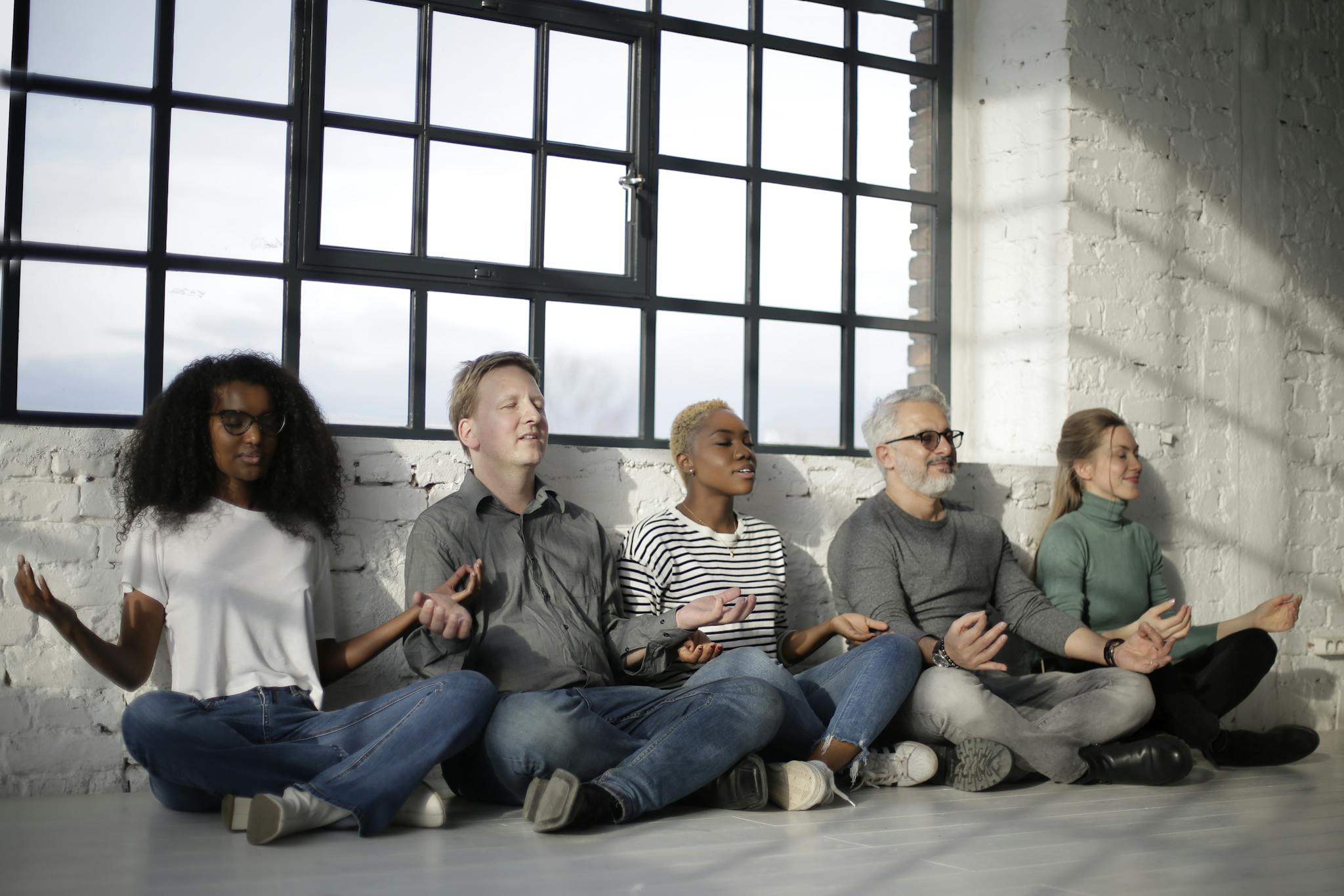 A diverse group of adults meditating together indoors in a tranquil loft environment.